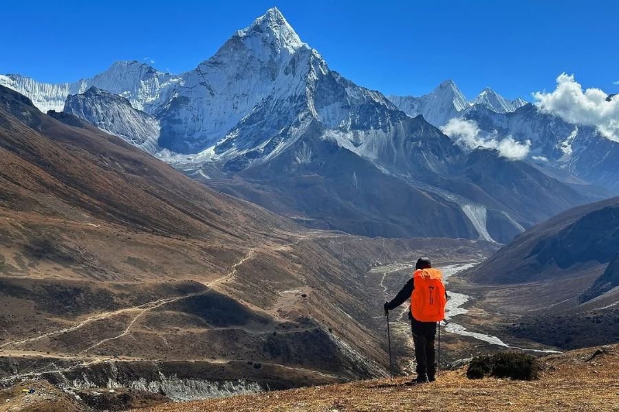 Solo trekker with orange backpack viewing Himalayan valley and peaks